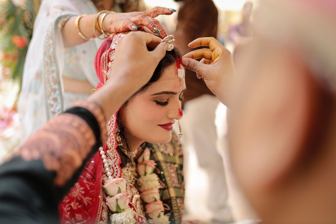 gallery-5 Close-up of an Indian bride in vibrant attire during a wedding ritual with detailed henna and jewelry.