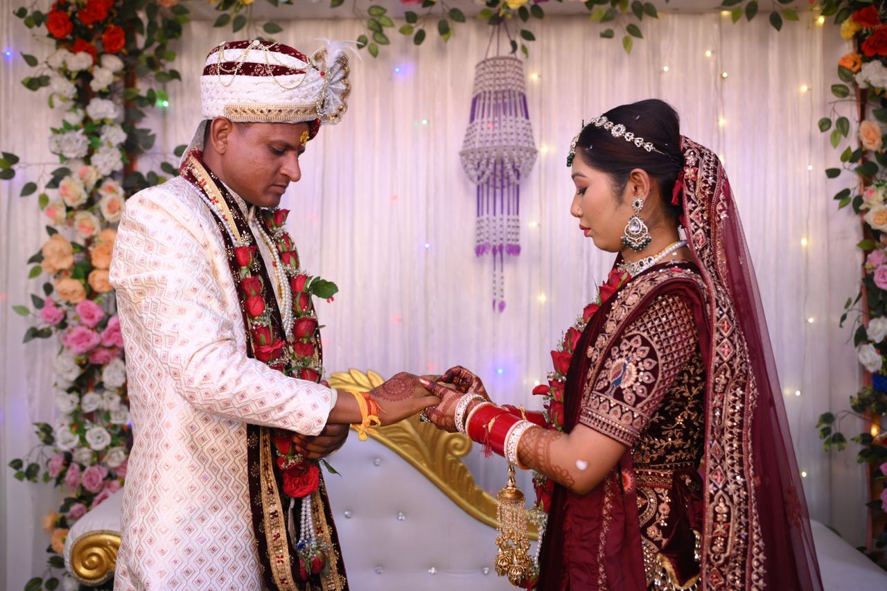 contact-img A couple exchanges rings in a traditional Indian wedding ceremony, adorned in vibrant attire with floral decorations.